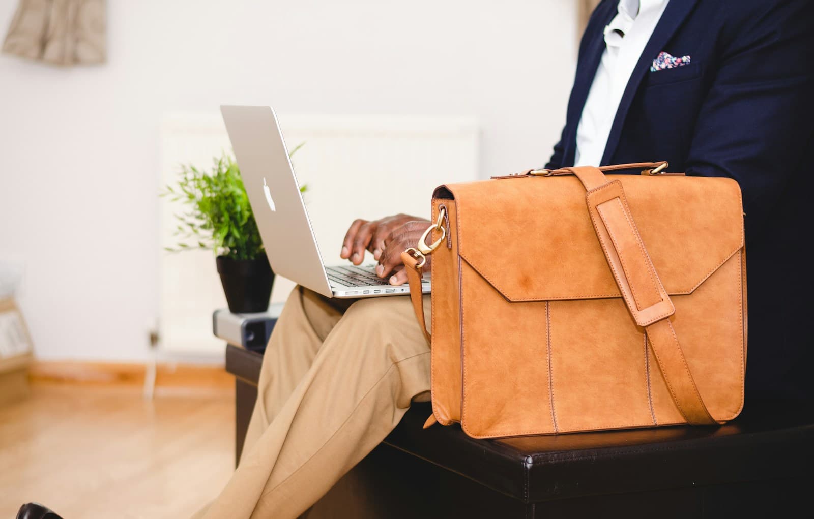 A person using a laptop beside a tan leather briefcase